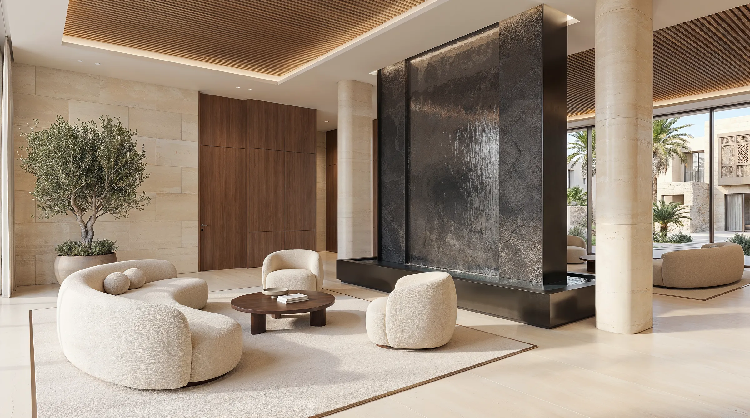 Lobby lounge with a dark stone water wall, boucle armchairs and an olive tree in a planter