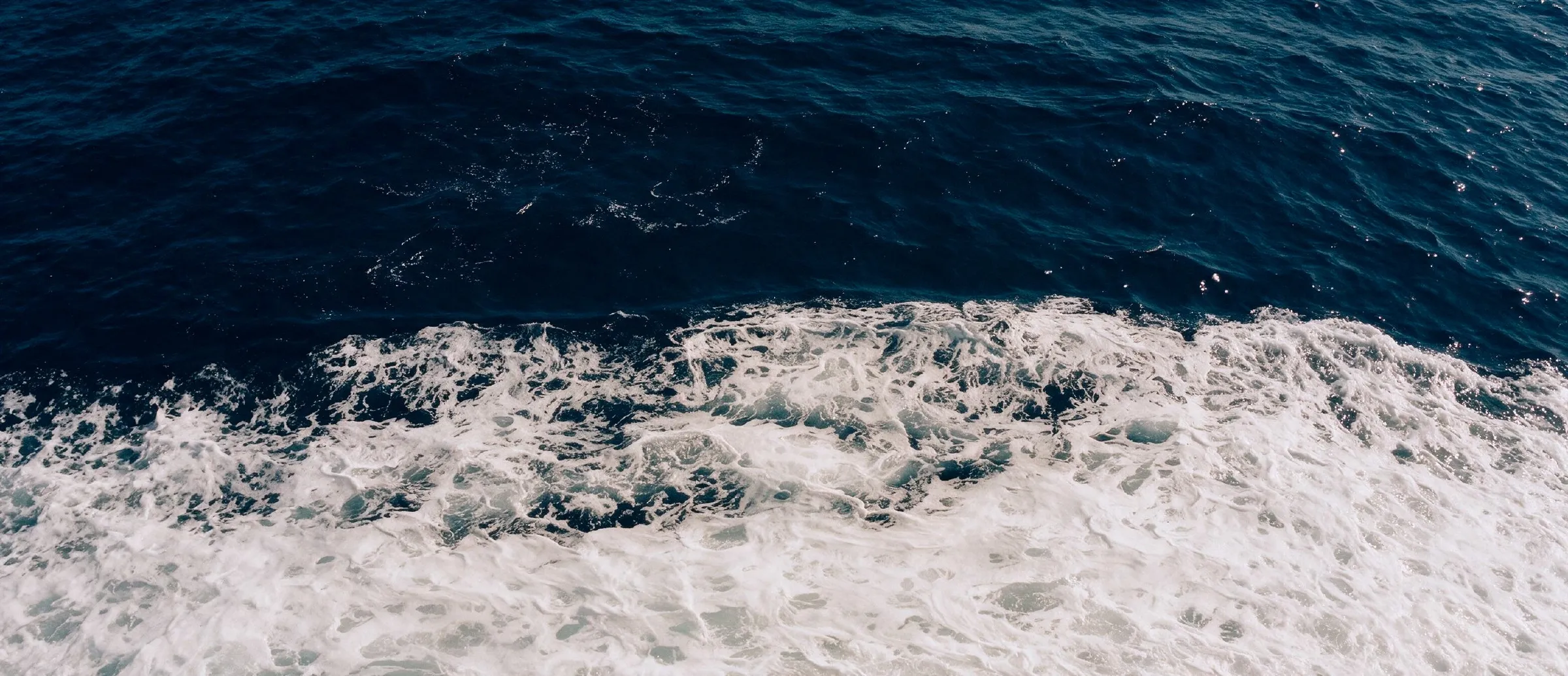 Surf breaking into deep blue water, seen from directly above