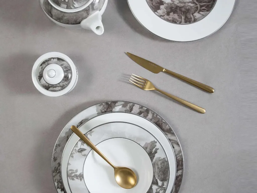 Place setting of patterned porcelain and gold cutlery laid out on stone